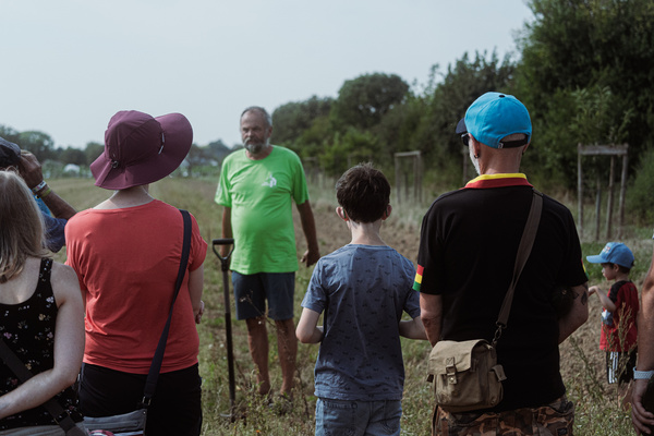 KI generiert: Eine Gruppe von Menschen steht auf einem Feld, ein Mann spricht zu ihnen.