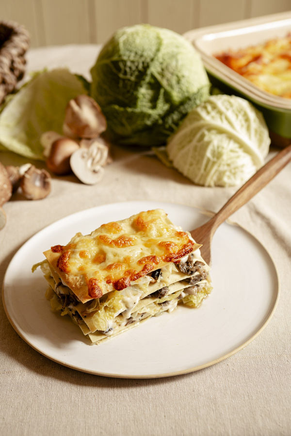 KI generiert: Lasagne-Stück auf einem Teller mit Wirsing und Pilzen im Hintergrund.