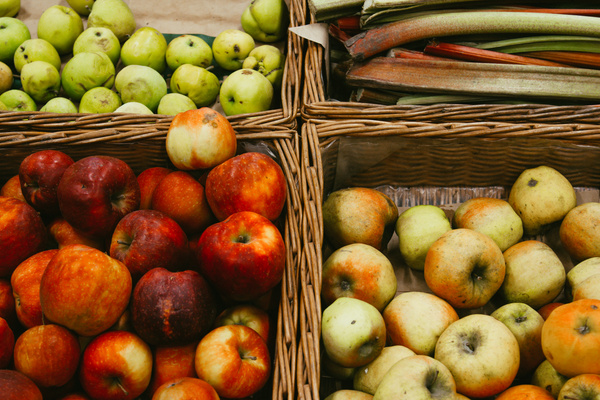 KI generiert: Verschiedene Apfelsorten in vier geflochtenen Körben auf einem Marktstand.