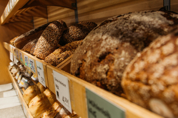 KI generiert: Regal mit verschiedenen Broten in einer Bäckerei. Preisschilder sichtbar.