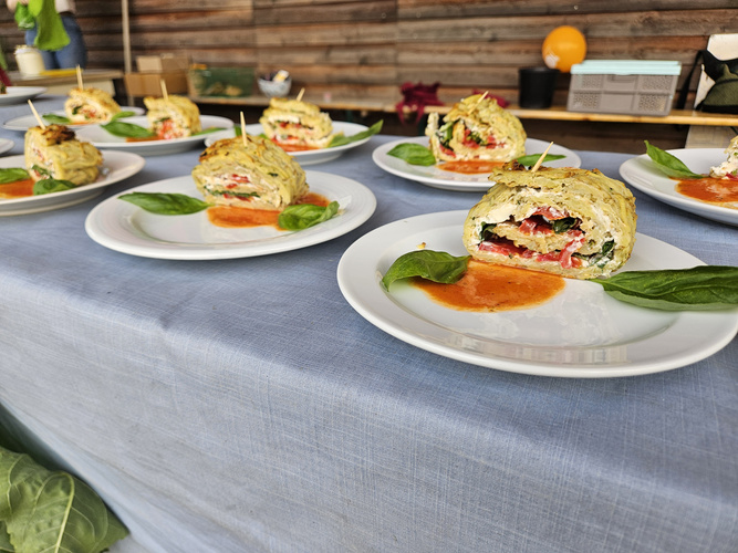 Kartoffel-Zucchini-Rolle mit Mozzarella, Tomate, Rucola & Knoblauchcreme auf einem Teller angerichtet mit Tomatensoße und 2 Basilikumblättern.
