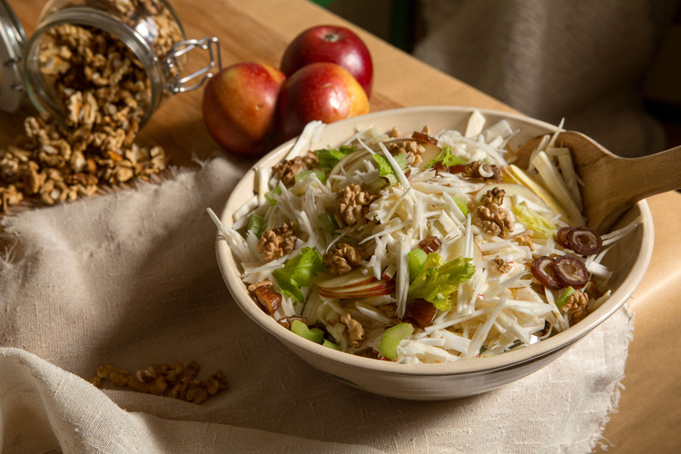 © Ökokiste e.V. Ein frischer Salat mit Sellerie, Äpfeln, Walnüssen und Datteln in einer Schüssel auf einem Tisch.