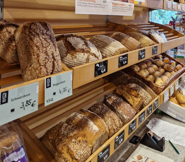 KI generiert: Frisch gebackene Brote in einem Regal, Preisschilder mit verschiedenen Brotarten und Preisen: "Schwarzbrot 3,85€".