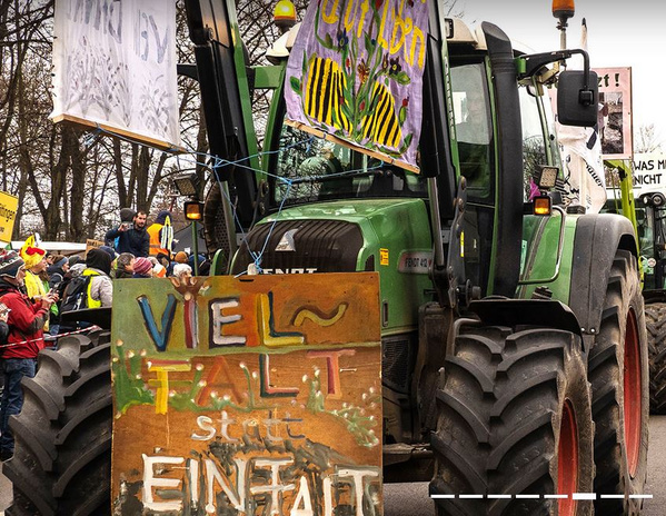 KI generiert: Das Bild zeigt einen Traktor mit Protestschildern, umgeben von einer Menschenmenge. Der Hauptinhalt ist eine Demonstration, die Vielfalt fördert.