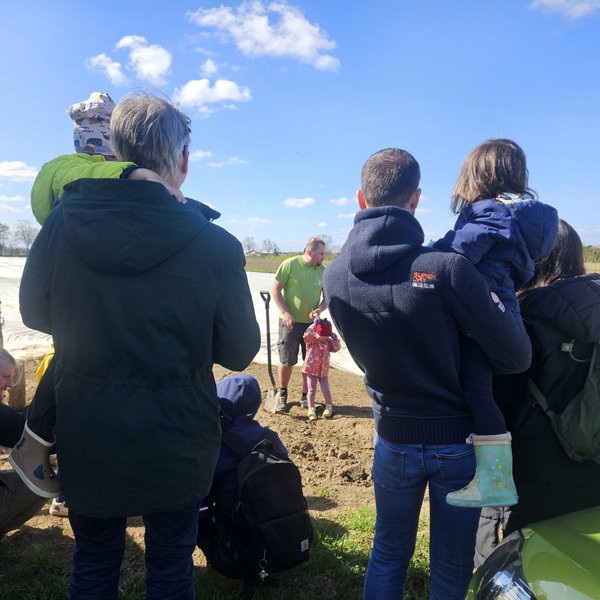 KI generiert: Eine Gruppe von Menschen steht auf einem Feld, ein Mann zeigt etwas.