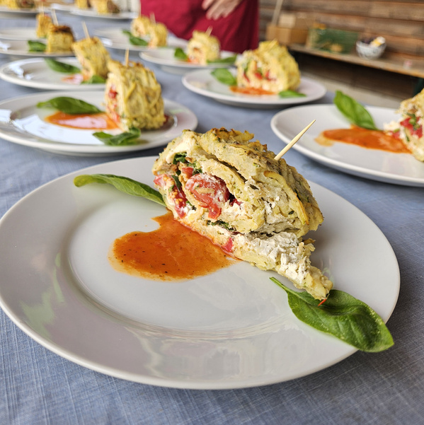Kartoffel-Zucchini-Rolle mit Mozzarella, Tomate, Rucola & Knoblauchcreme auf einem Teller angerichtet mit Tomatensoße und 2 Basilikumblättern.