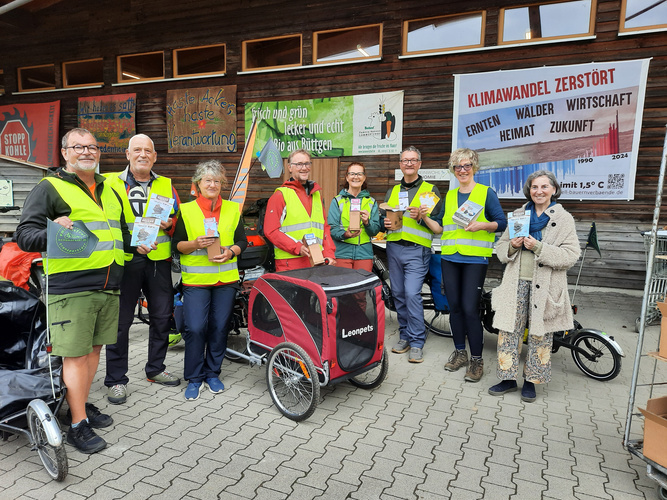 KI generiert: Gruppe von Menschen in gelben Westen mit Flyern vor Bannern zu Klima und Bio-Lebensmitteln.