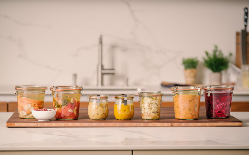 KI generiert: Mehrere Einmachgläser mit verschiedenem eingelegtem Gemüse auf einem Holzbrett in einer Küche.