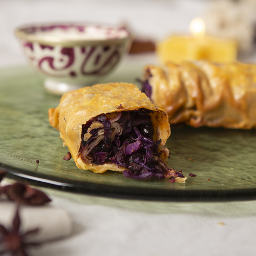 KI generiert: Ein Strudel mit Rotkohlfüllung auf einem Teller, im Hintergrund verschwommenes Geschirr.
