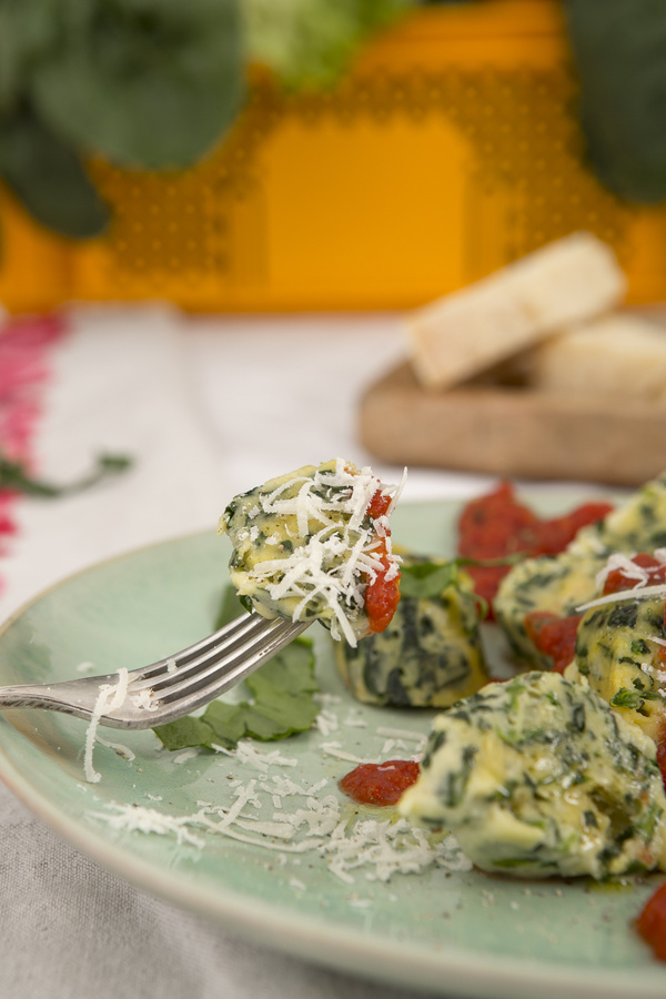 KI generiert: Leckeres Gericht mit Spinatklößen, Tomatensoße und geriebenem Käse auf einem grünen Teller.