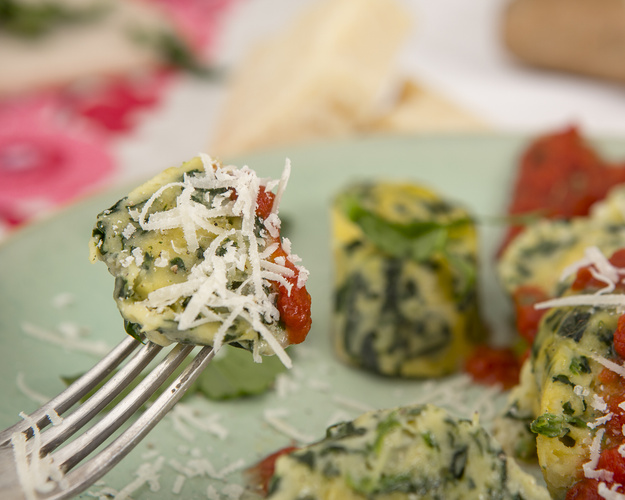 KI generiert: Gabel mit Spinat-Gnocchi und Tomatensauce, bestreut mit geriebenem Käse auf einem Teller.