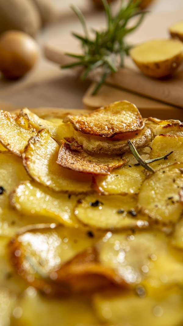 KI generiert: Gebackene Kartoffelscheiben mit Rosmarin, im Hintergrund weitere Kartoffeln.