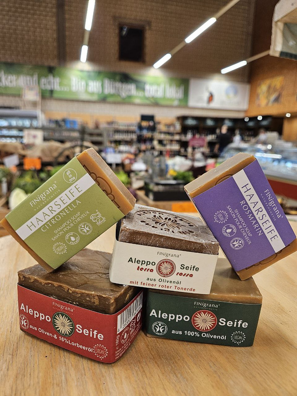 KI generiert: Seifen in einem Geschäft: Aleppo Seife, Haarseife Citronella, Haarseife Rosmarin.