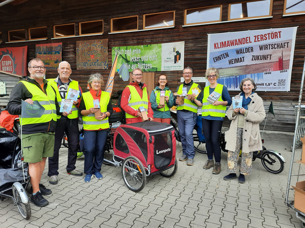 KI generiert: Eine Gruppe von Menschen in Warnwesten mit Infomaterial, im Hintergrund Banner gegen Klimawandel.