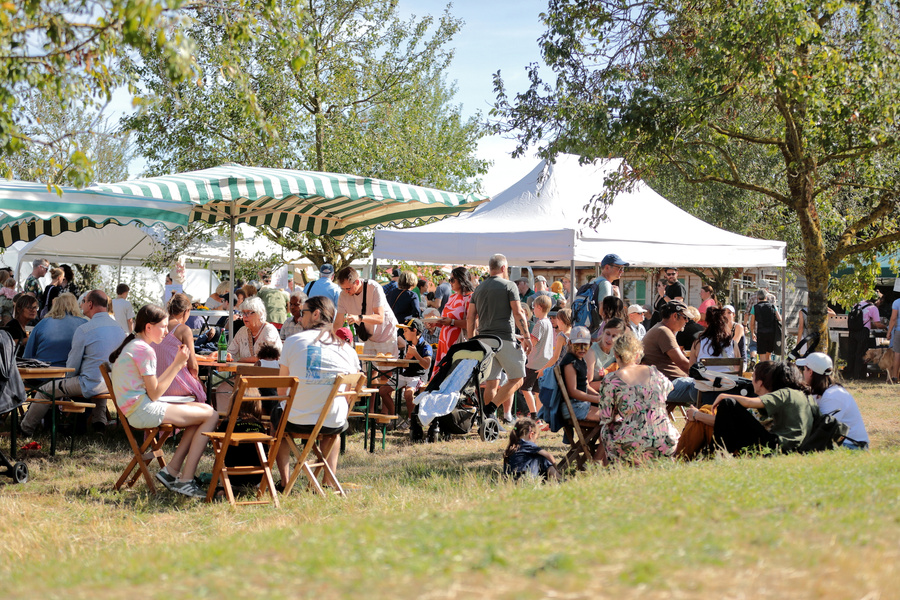 KI generiert: Menschen sitzen und stehen unter Pavillons auf einem sonnigen Outdoor-Event.